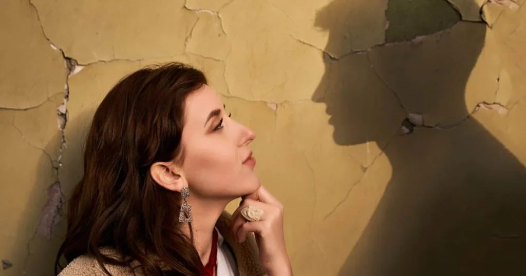 A woman stands before a wall, her shadow visible, dreaming about the same person romantically, immersed in contemplation.

