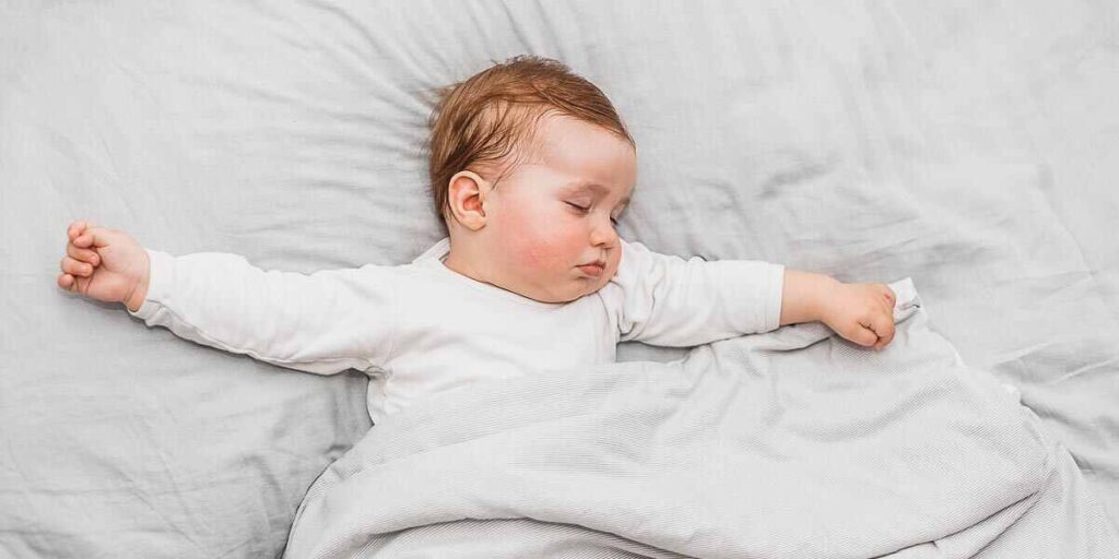 A peaceful baby sleeping in a bed, covered with a white blanket, symbolizes the theme of "Understanding Dreams of Your Child Dying."

